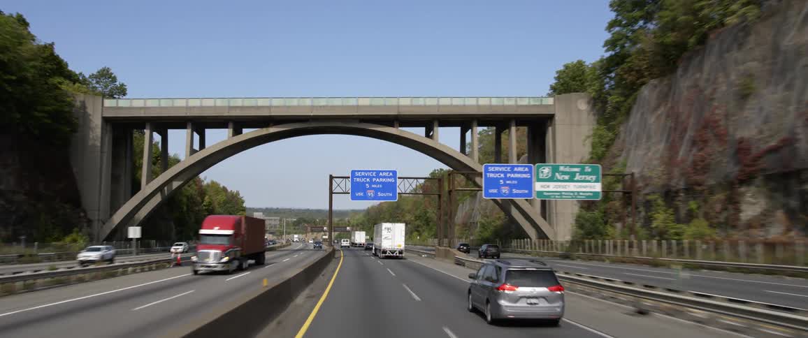 Traffic movies along a highway surrounding by stone cliffs under a clear blue daytime sky