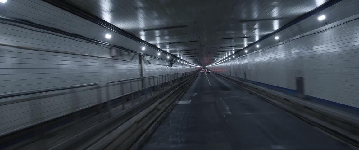 A long vehicle tunnel with white tiles and lights that has 2 lanes for traffic