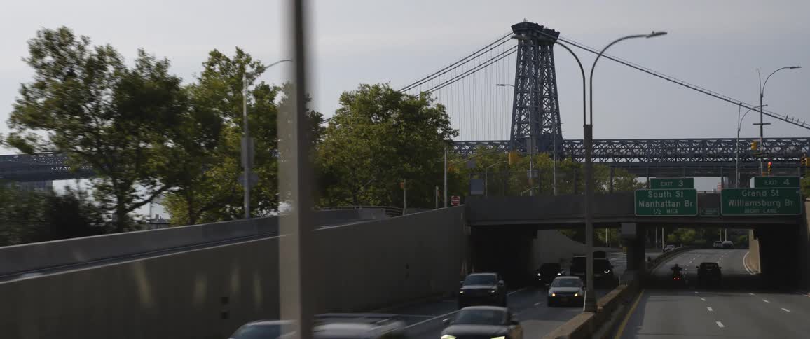 A street with vehicles in traffic passing trees and viewing a large steel bridge
