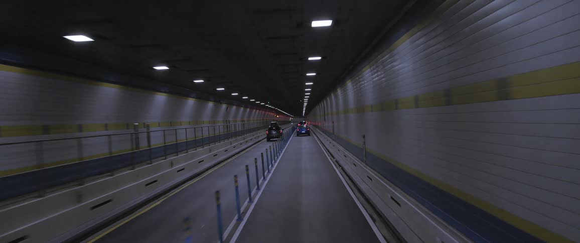 Vehicles drive through tunnel lined with gray tiles past sign under lights