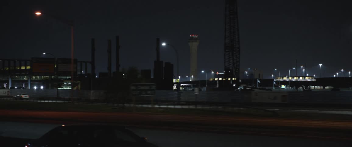 Cars driving past a factory with a skyline in the far distance
