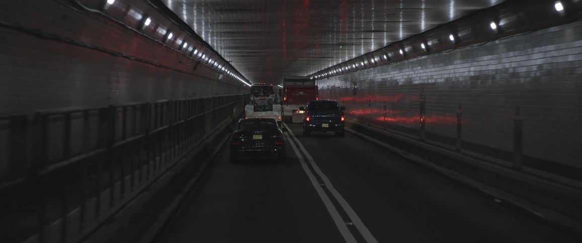A car and a truck drive down a tunnel behind firetrucks with flashing lights