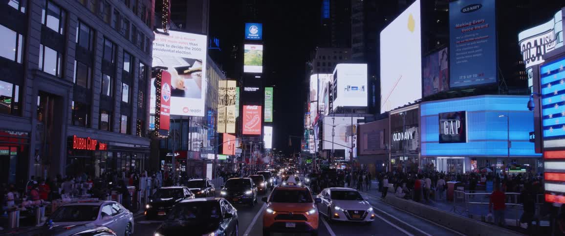 A street in a city with buildings and electronic signage and traffic at night
