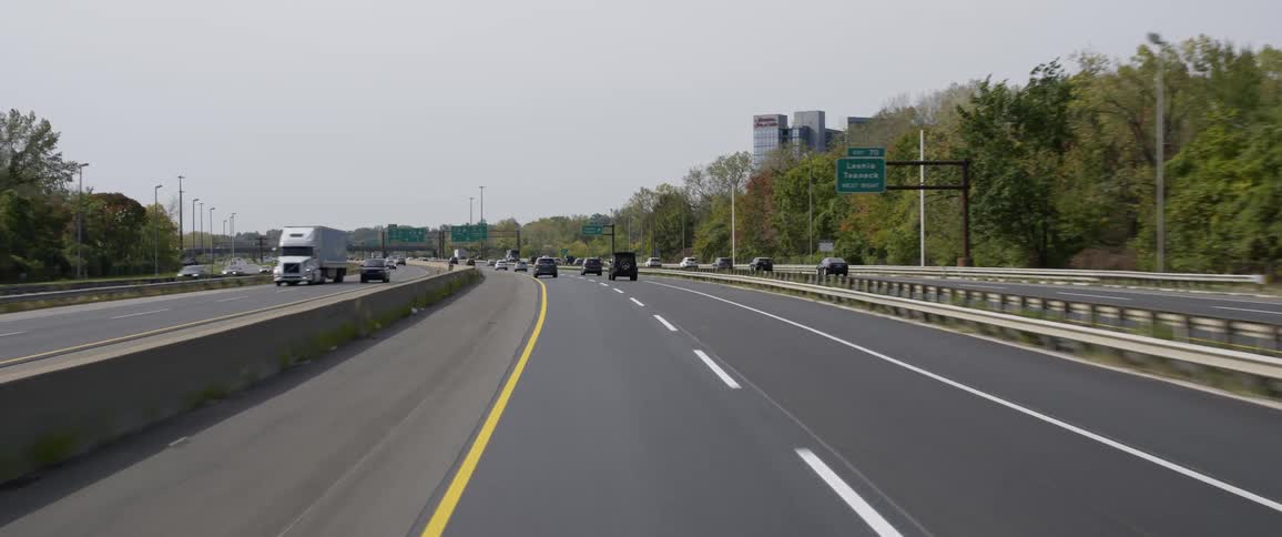 A highway with vehicles in traffic with trees and buildings on the side of the highway on a clear day