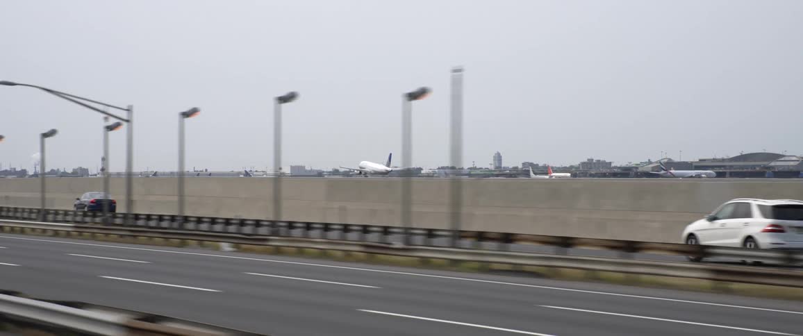 Traffic travels along a highway beside an airport where an airplane is making a landing