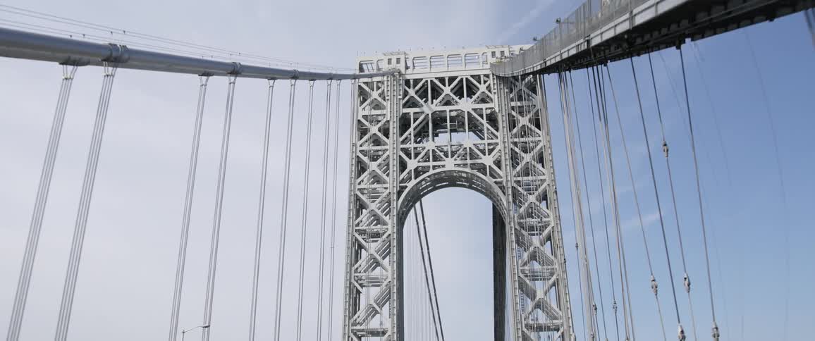 Traffic moves under the large tower of a suspension bridge on a sunny day