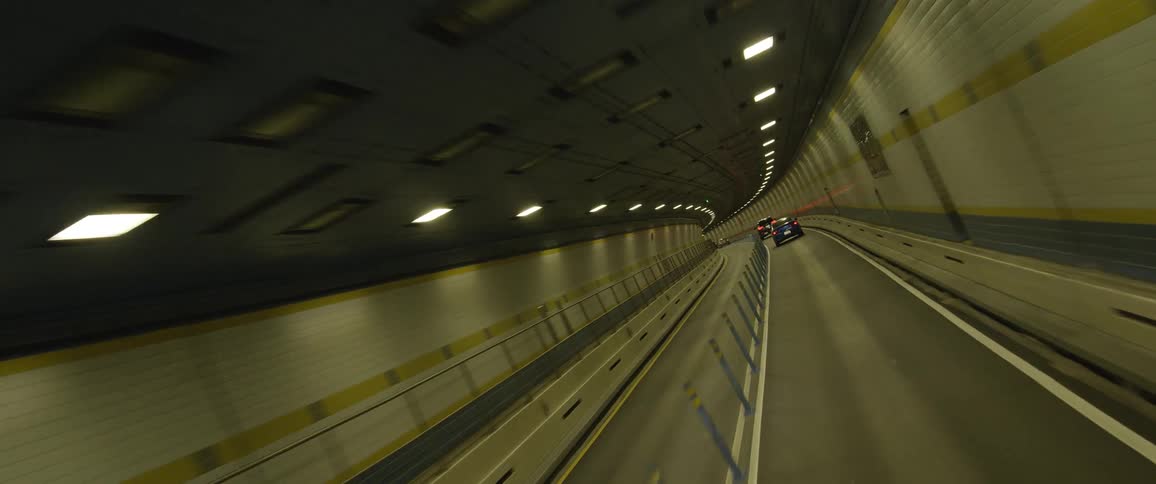 Cars drive down a winding tunnel in urban area
