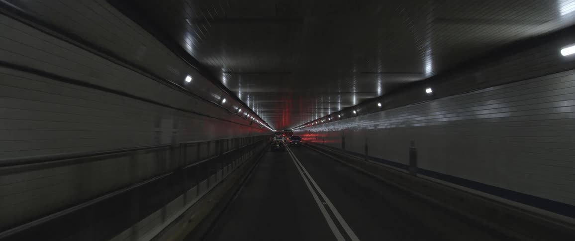 Taillights and ceiling lights reflect from tile lining tunnel surrounding street