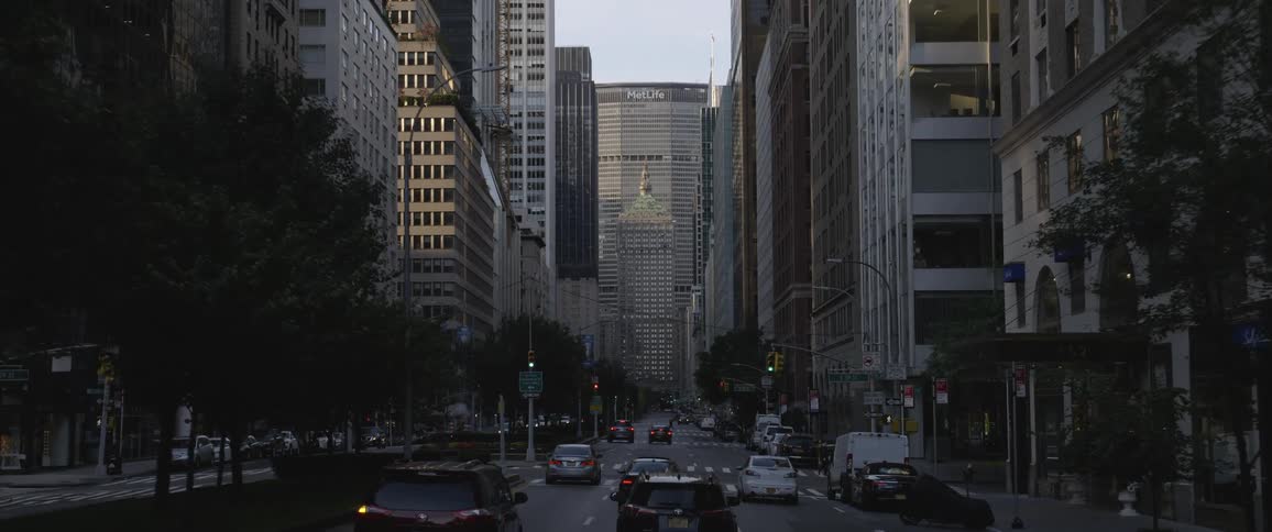 Cars drive down the road in a downtown urban setting while people cross the road