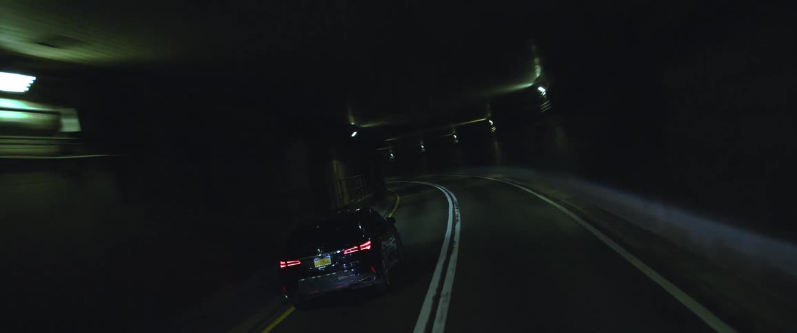 Car drives through curvy tunnel with a few lights around the top