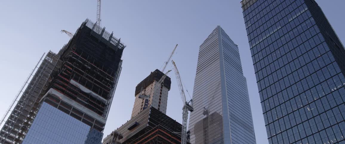 A pair of completed skyscrapers next to a pair of skyscrapers under construction in a metropolis under a clear daytime sky