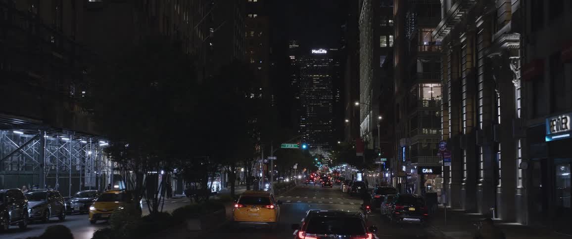 Traffic moves along a city street next to buildings and trees