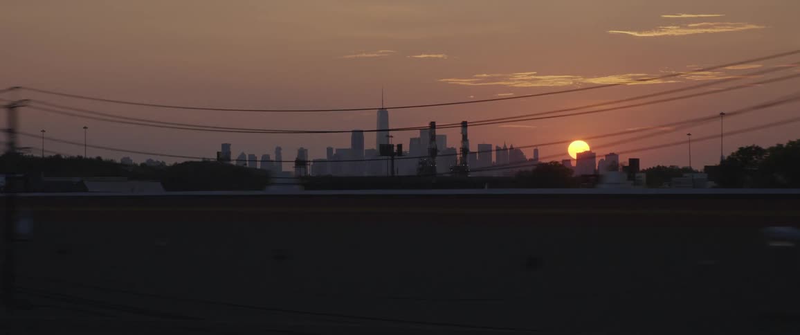 City area with a lot of parked cars at sunset behind powerlines and billboards and in front of a city skyline