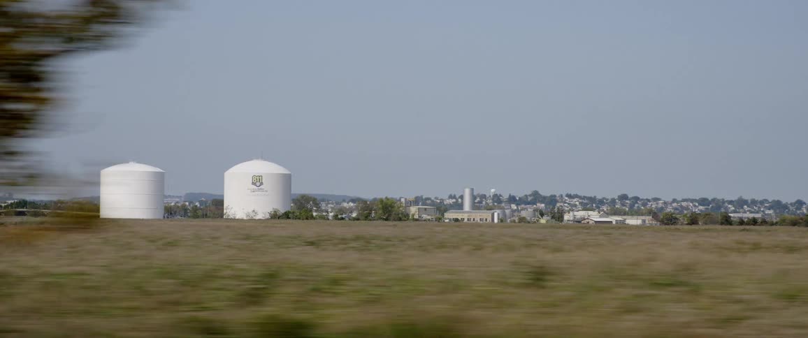 Silos and factory on the plains near a river filmed from a moving vehicle