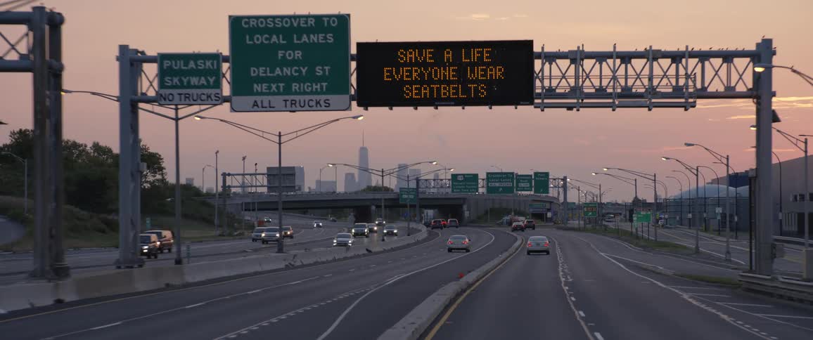 Vehicles drive down a highway at sunset either toward or away from a city