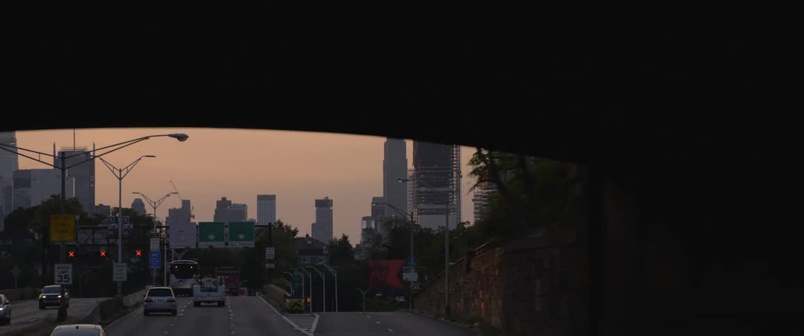 Traffic passes under bridge heading to and from city downtown under red tinted overcast sky
