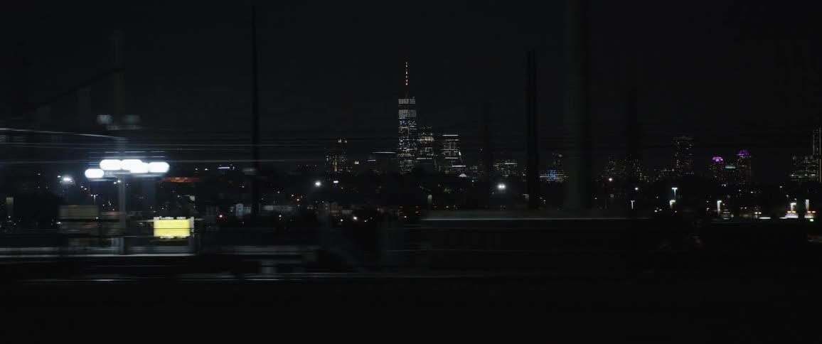 Moving on a road with a skyline of a city at night and passing a subway or train station