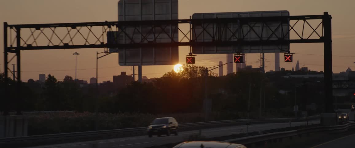 Cars with illuminated headlights traveling on a city freeway at sunset