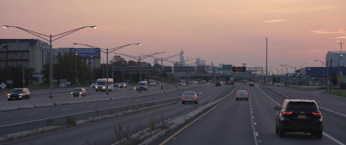 Cars are driving on a highway near a city at dusk