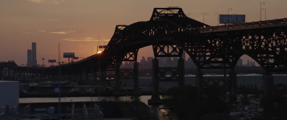 A bridge in front of the new york city skyline at sunset