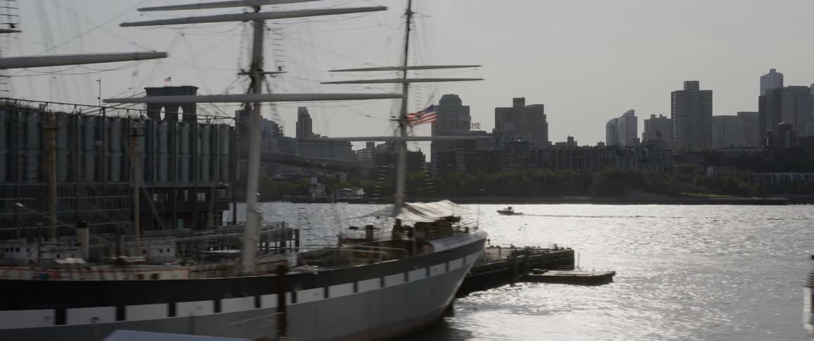 Boats at a pier and a boat driving in the water with the city skyline in the distance