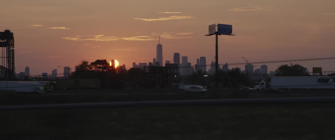 Sun setting behind the new york city skyline at sunset filmed from the highway