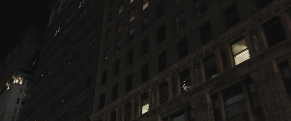 Lights shine upward on building at night as lights shine from windows