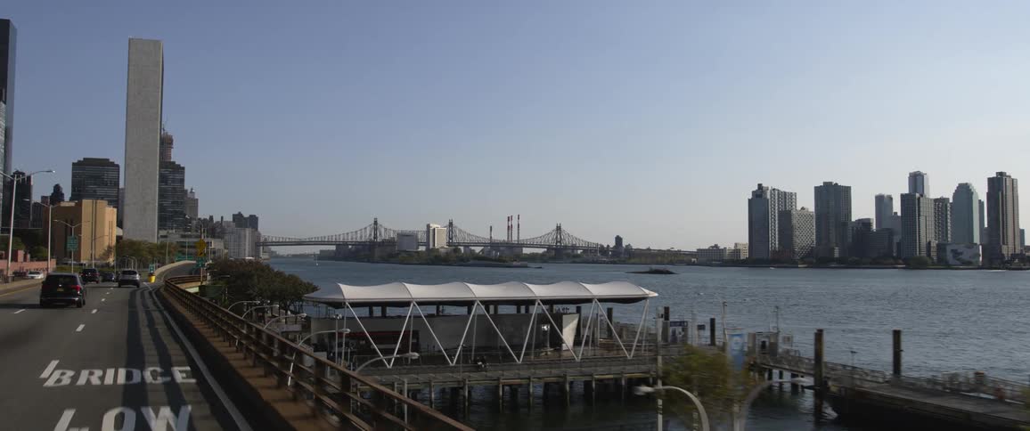 Cars driving a long a road on the shore with a city skyline across the water