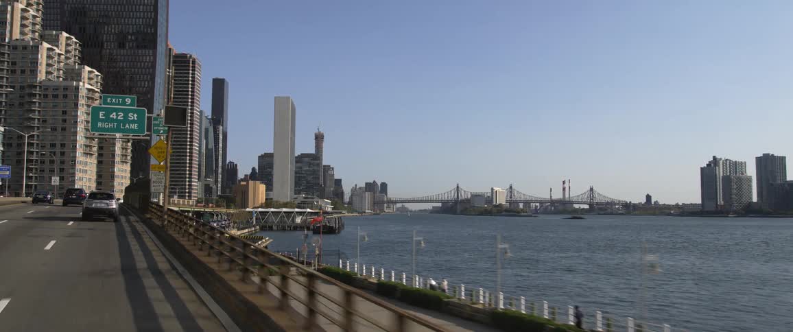 Vehicles drive on a highway alongside a river that leads to downtown