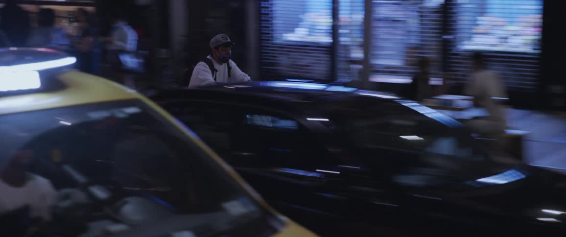 A man rides a bike on a busy city street passing storefronts at night