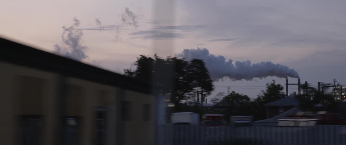 Smoke billowing from the smokestack of a factory floats over the buildings of a town at sunset