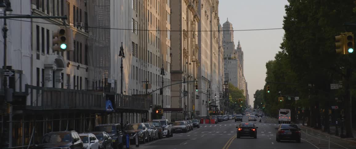Cars driving down a city street with office buildings and pedestrians walking
