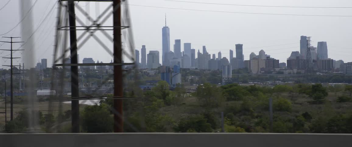 Vehicles drive past a power plant on the shore with a city skyline in the distance