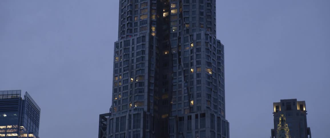 A tall skyscraper looms over the surrounding buildings in a metropolis in the evening
