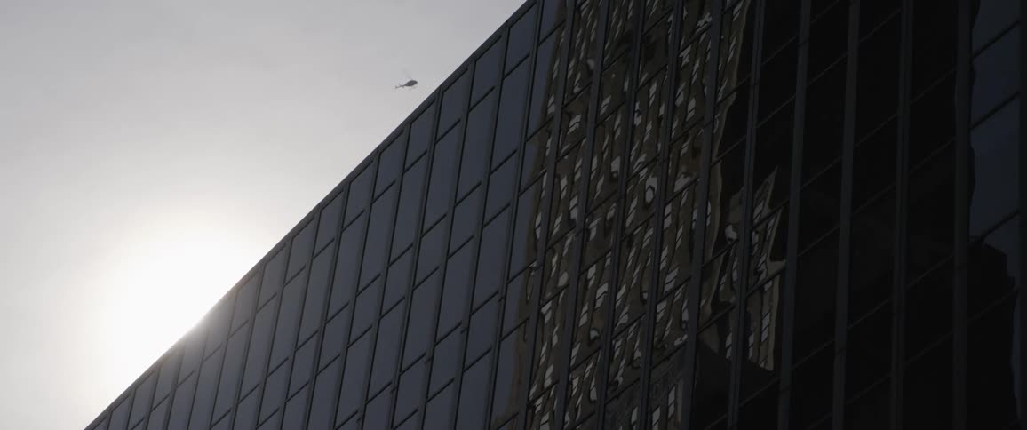 A helicopter flying over a large city building on a sunny day
