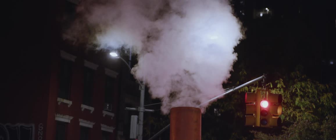 Steam venting from a chimney in the middle of the citys downtown at night