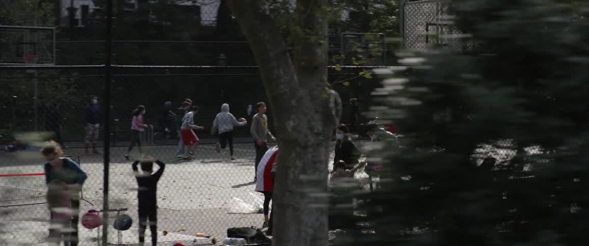 People at a public park playing basketball and riding scooters and standing on the sidelines