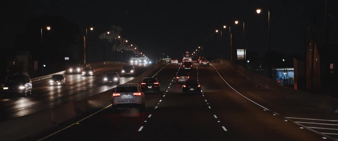 Cars drive down highway at night going both ways in six lanes