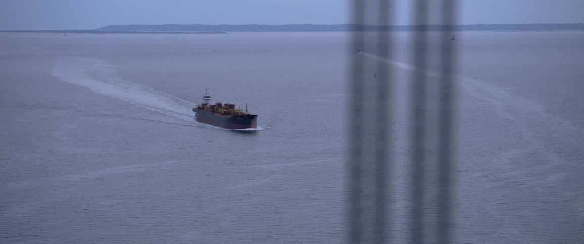 A cargo shipping boat on a river filmed from a bridge at morning