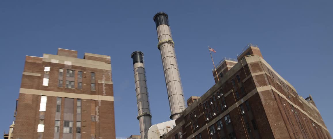 Tall grey chimneys over the brick building of a factory under a blue sky