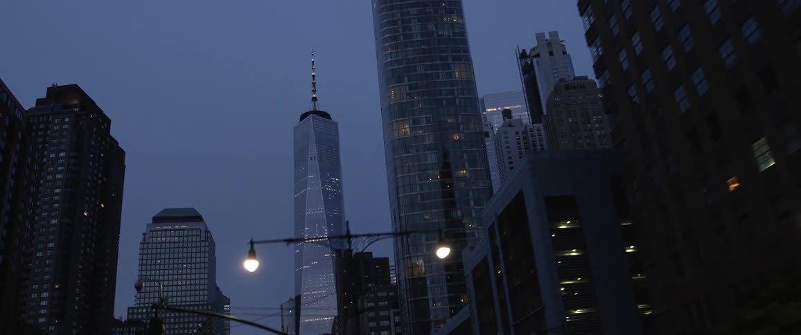 Tall buildings and skyscrapers loom over a street through a metropolis at night