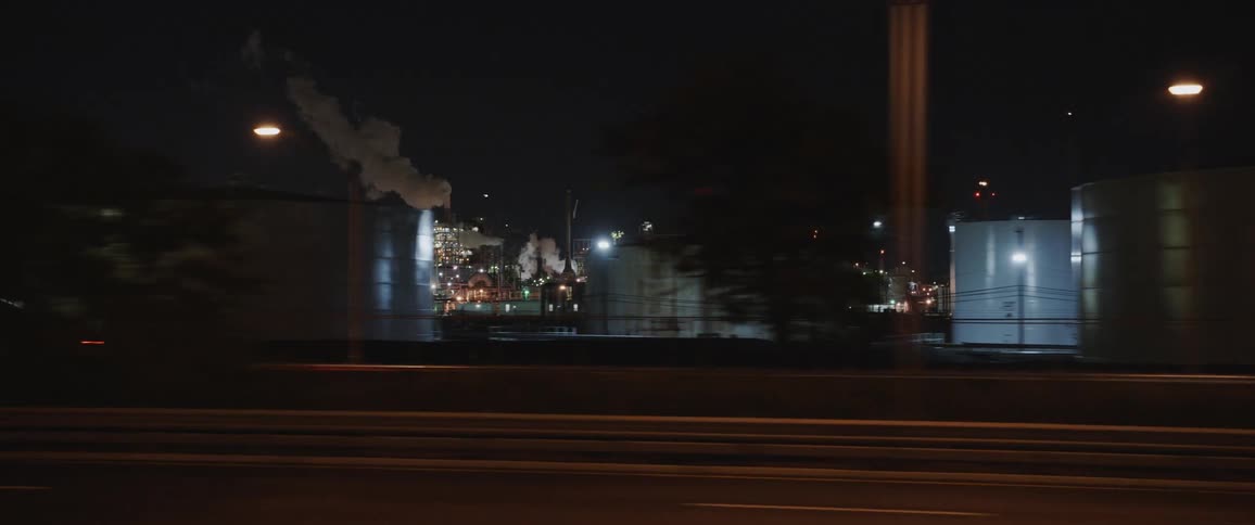 Driving past a gas station city skyline and an industrial park at night