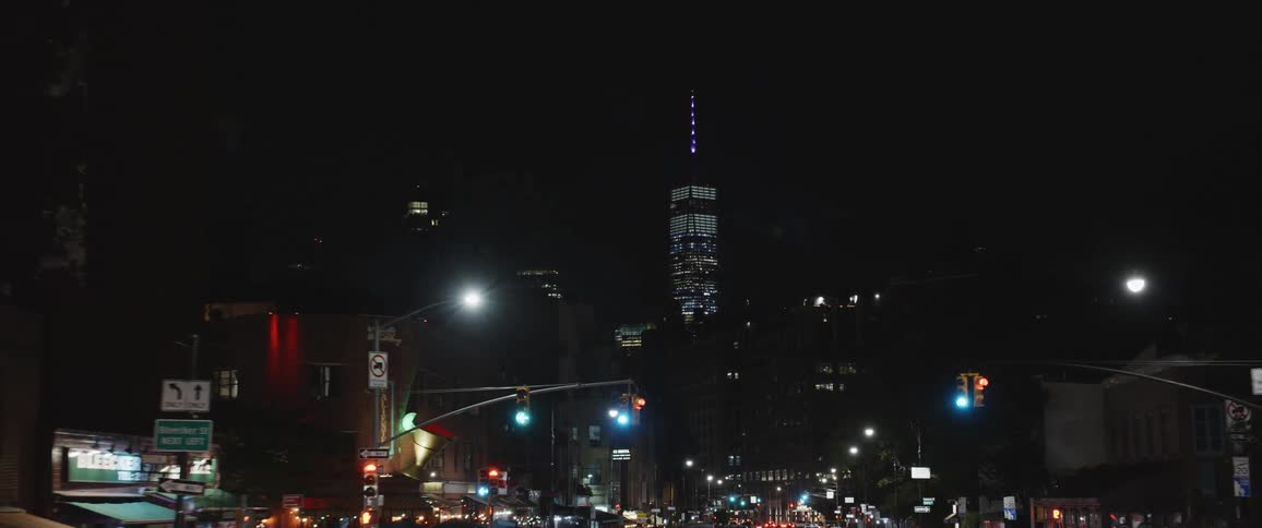 A skyscraper in a city at night with buildings and a busy street at its feet