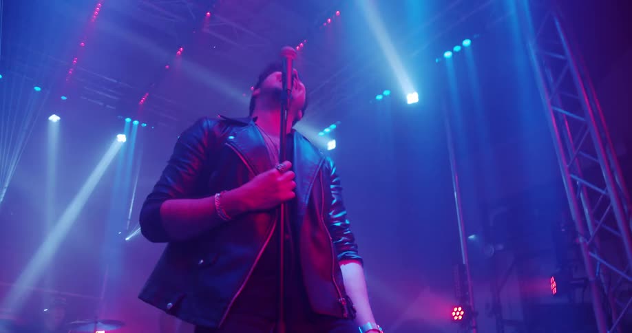 A man singing on stage with his band behind him