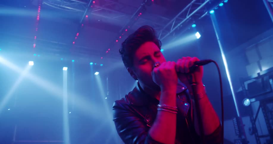 A lead singer sings while guitar players play music on a well lit stage