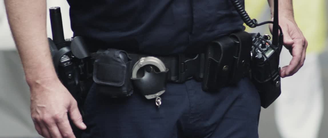 A uniformed police officer's belt holding a radio, handcuffs and gun