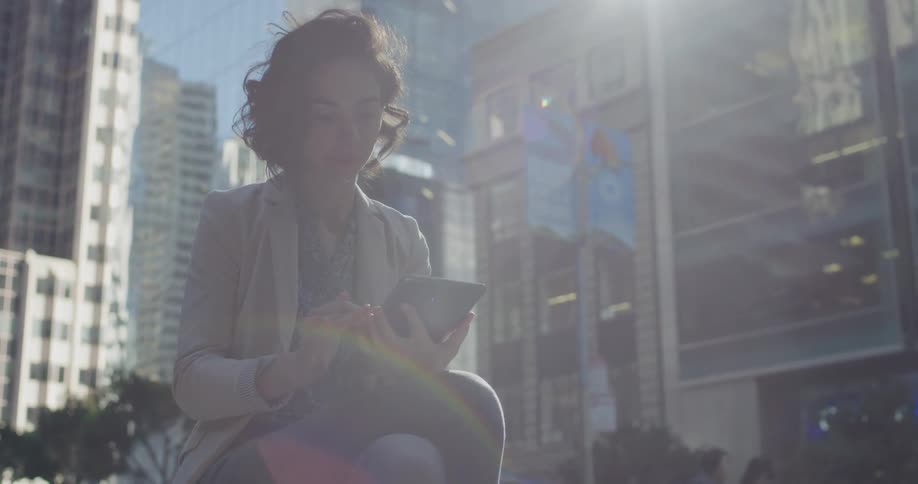 A caucasian woman dressed in business attire sitting scrolling through her tablet in a downtown metro area