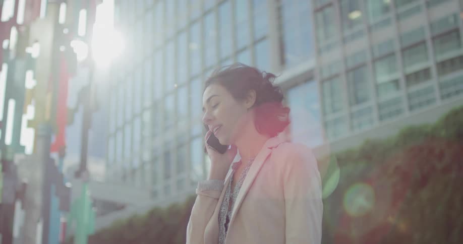 A woman standing outside talking on a smart phone with a building in the background