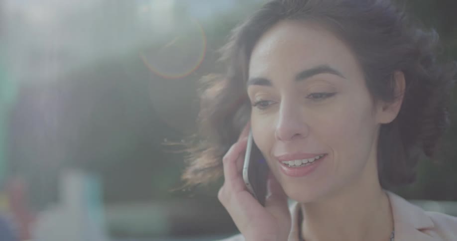 A woman talking on a smart phone with a hedge in the background