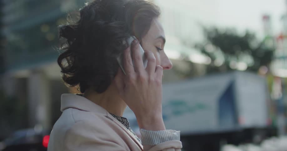 A woman talks on her phone while pacing on a busy city street as traffic passes by
